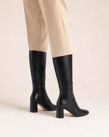Women's black knee-high boots with a broad block heel, rear three-quarter view.